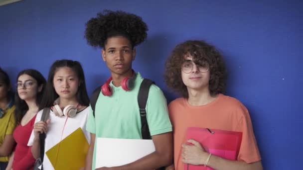 Портретная группа друзей-подростков, смотрящих на камеру, стоящую над синей стеной в старшей школе — стоковое видео