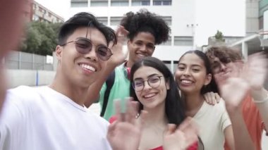 Asyalı genç adam ve bir grup etnik çeşitlilikte genç arkadaş kameraya bakarak selfie çekiyorlar. Ortaokuldaki mutlu öğrenciler merhaba diyor. 