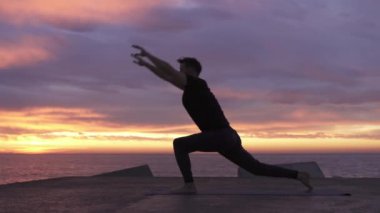 Genç atletik adam güneş doğarken okyanusun önünde yoga pozu veriyor. Sağlıklı ruhsal sabah yoga rutini