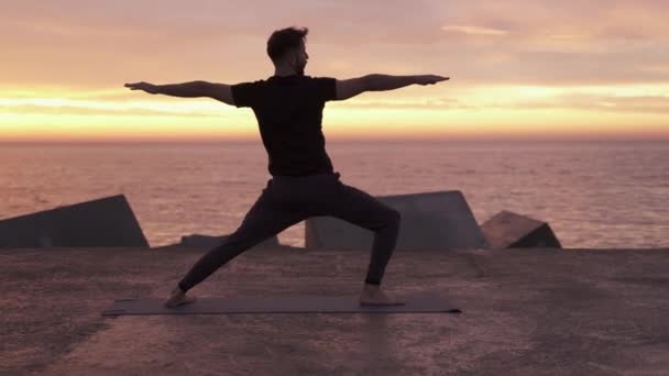 Young athletic man performing yoga pose in front of the ocean at sunrise. Healthy spiritual morning yoga routine — Stock Video