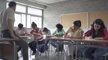 Ortaokul 'da Oturma Sınavı Öğrencileri. Çok ırklı odaklı öğrencilerden oluşan bir grup öğretmen denetimi altında yazım sınavı