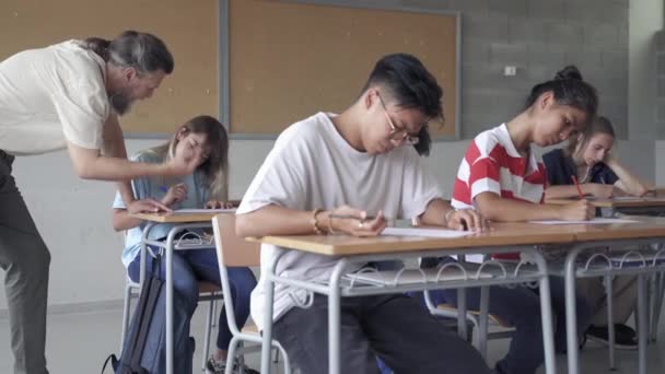 Azjatycki student zdający egzamin i profesor wyjaśniający ćwiczenia nastolatkowi w klasie gimnazjalnej — Wideo stockowe