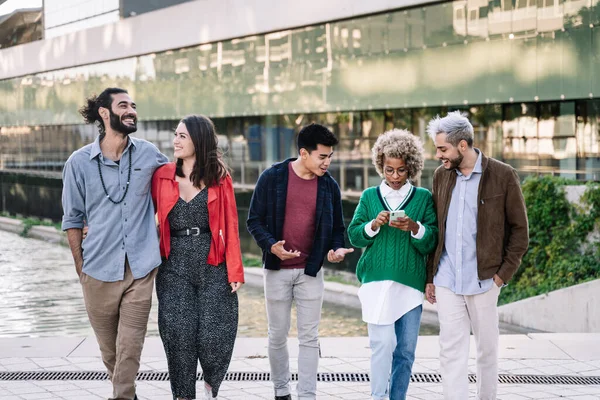 En gruppe trendy unge venner som nyter tiden i byen. Multi etniske bander som går og har det gøy med å se på smarttelefoner. Vennskap og livsstil – stockfoto