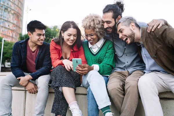 Kosmopoliittinen ryhmä onnellisia monikansallisia ystäviä jakamassa sosiaalisen median sisältöä älypuhelimella. Monipuolinen sekarotuisia nuoria hauskaa käyttää internetiä moderni kaupunki, Barcelona — kuvapankkivalokuva