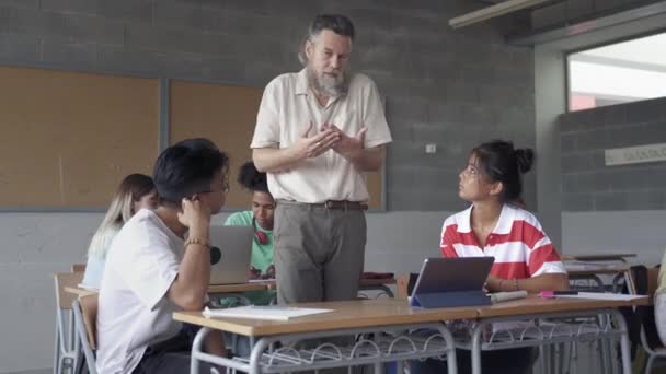 Professor assistindo estudantes asiáticos em sala de aula multi étnica. Professor com barba explicando assunto para alunos adolescentes durante a palestra da Faculdade de Ensino Médio — Vídeo de Stock