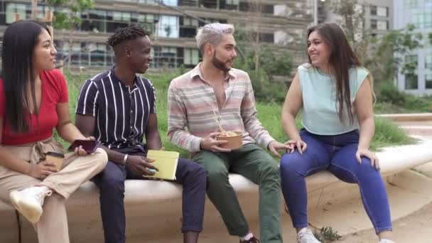Grupa młodych przyjaciół z wielu grup etnicznych, cieszących się rozmową podczas jedzenia, bierze uliczny posiłek w parku miejskim — Wideo stockowe