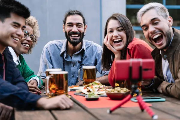 Groep multiraciale vrienden genieten van eten en bier drinken terwijl ze online videobellen met een mobiele telefoon in de brouwerij bar om verjaardag te vieren - Focus op de mens gezicht — Stockfoto