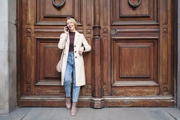 Resmi olarak gülümseyen zarif bir kadın arkadaşlarıyla cep telefonunda hoş sohbetler yapıyor. Cep telefonuyla konuşan mutlu çekici bir kadın. Ahşap evin ya da otelin kapısında duruyor.