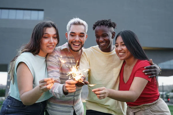 Heureux amis multiraciaux profiter de la célébration avec des feux d'artifice scintillants. Focus sur l'homme africain — Photo