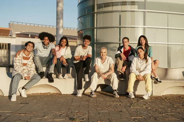 Ryhmä erilaisia teini yliopiston opiskelija ystäviä istuu moderni kaupunkien alueella auringonlaskun nauttia hengailla yhdessä — kuvapankkivalokuva