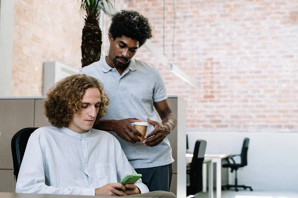 To forskjellige kreative mannlige medarbeidere som bruker smarttelefon i arbeidstiden på kontoret – stockfoto