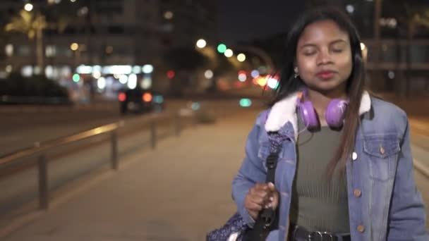 Jovem afro-americana estudante mulher andando na cidade à noite. Mulher latina confiante e feliz na rua — Vídeo de Stock