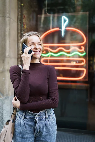 Onnellinen nainen soittaa ystäville sisäänkäynnin hampurilainen baari, puhumme hengailla viikonloppuna suunnitelma — kuvapankkivalokuva