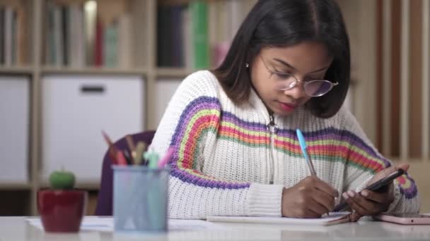 Afrikansk latinamerikansk ung kvinna med glasögon använder miniräknare och skriver anteckningar studerar för universitetet Tentor — Stockvideo