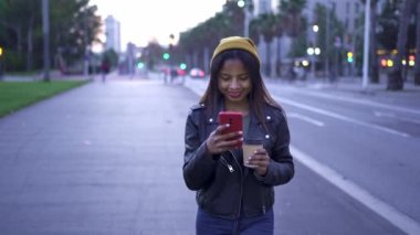 Tasasız genç Afro-Amerikan Kadın şık deri ceketli. Akşamları akıllı telefonuyla mesajlaşıyor.