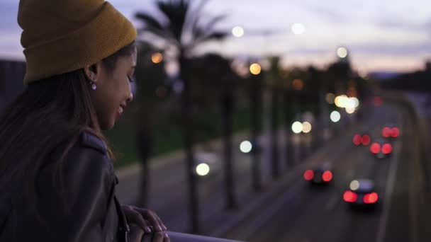Молода афроамериканська жінка, яка дивиться з натхненням на міське шосе з рухомими ліхтарями машин вночі готові до пригод і подорожей — стокове відео