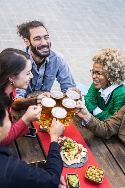 Group of happy multiethnic friends toasting beer mugs in a bar to celebrate friendship — Stockfoto