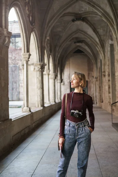 Pensive female traveler with vintage camera visiting ancient monastery church in European city — kuvapankkivalokuva