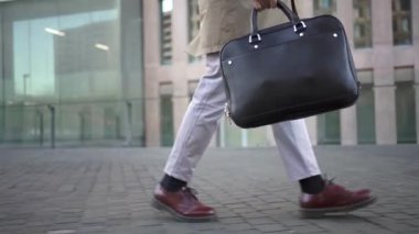 Confident young lawyer businessman with briefcase full of documents calling with mobile phone while walking to meeting with clients in the city