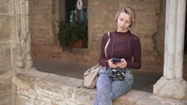 Kameralı kadın gezgin, Avrupa 'daki antik bir anıtta çevrimiçi turizm bilgilerini aramak için akıllı telefon kullanıyor.