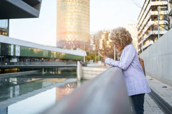 Profesjonell fremgangsrik afroamerikansk kvinne som står i moderne by og bruker mobilsmarttelefon etter jobb – stockfoto