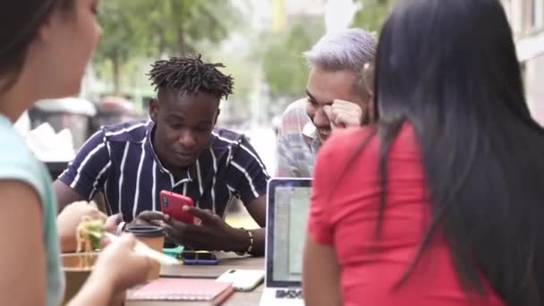 De jeunes amis étudiants qui travaillent sur un ordinateur portable pendant que leurs collègues mangent sainement sortent de la nourriture en plein air dans la ville — Video