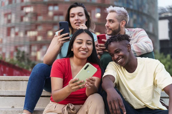 Des amis latino-américains et afro-américains partageant du contenu de médias sociaux sur téléphone intelligent. Divers jeunes gens s'amusent à utiliser Internet dans une ville moderne — Photo