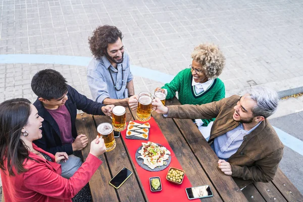 Onnelliset ystävät nauttivat aikaa yhdessä ottaa juomia ja ruokaa paahtamalla olutta juhlia ystävyyttä — kuvapankkivalokuva