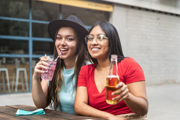 Kaksi naispuolista latinoystävää erasmus-opiskelijaa, joilla on hauskaa yhdessä juomassa olutta ja juomia viikonlopun viettämiseksi töiden jälkeen — kuvapankkivalokuva