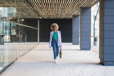 Ofis bölgesinde yürüyen kendine güvenen siyahi kadın gülümseyen güçlü Afro-Amerikan kadın yönetici başarılı bir şirket kariyerinin tadını çıkarıyor.