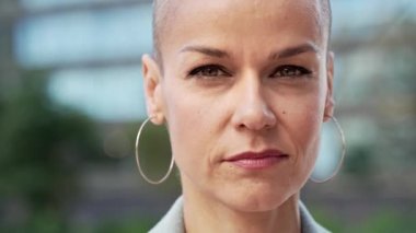 Saçı tıraşlı, kendine güvenen şık bir kadının yakın portresi. Güçlü, güçlü bir dişi kameraya bakıyor. 