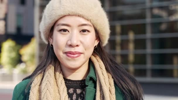 Resmi kışlık kıyafetli genç gülümseyen Asyalı kadın iş yerinin dışında kameraya bakıyor. — Stok video