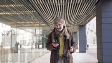 Üst düzey profesyonel iş adamı ofisin dışında yürürken cep telefonu mesaj uygulamasını kontrol ediyor.