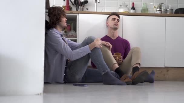 Gay pareja sentado en la cocina piso tener un romántico conversación mientras bebiendo un Caliente bebida — Vídeos de Stock