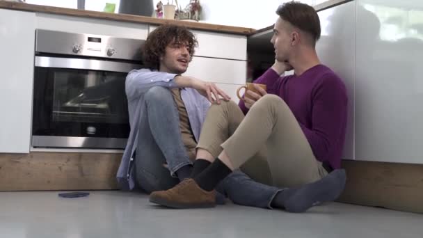 Dos amigos gay sentados en el piso de la cocina disfrutando del tiempo juntos teniendo una conversación romántica en casa — Vídeos de Stock