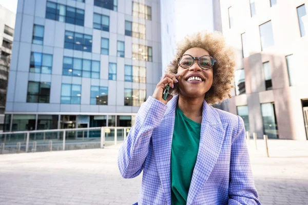 Muodikas musta bisnesnainen, jolla on silmälasit puhelinsoitossa rahoitusalueella. Luova nainen ammattilainen kaupungissa — kuvapankkivalokuva