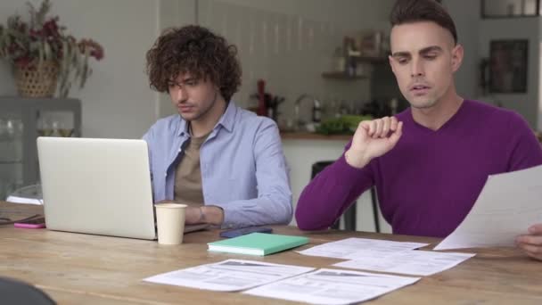 Jeune couple gay gérant les finances, examinant leurs comptes bancaires à l'aide d'un ordinateur portable à la maison. Amis faire de la paperasserie ensemble, payer des impôts en ligne — Video