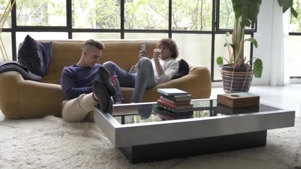 Fiatal férfi meleg pár ellazult a kanapén élvezi a digitális technológia csatlakozik a közösségi média okostelefonok otthon — Stock videók
