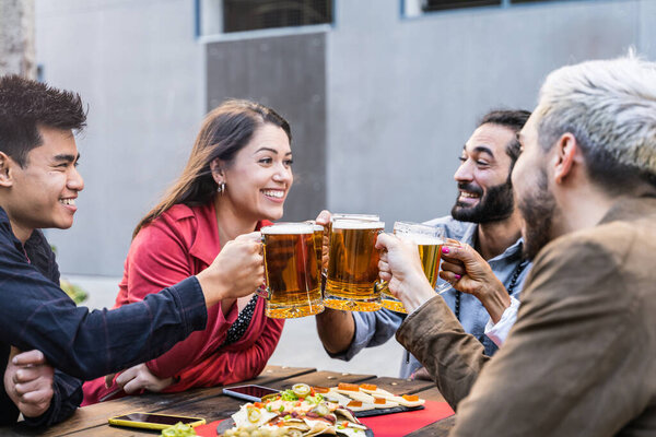 Group of multicultural friends drinking and toasting beer at brewery bar restaurant - Happy people having fun at outdoors tapas bar