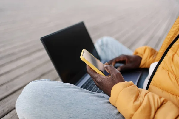 En afrikansk-amerikansk mann som jobber med en bærbar PC med gul mobil for å verifisere kontoen. Frilanser tilknyttet online – stockfoto