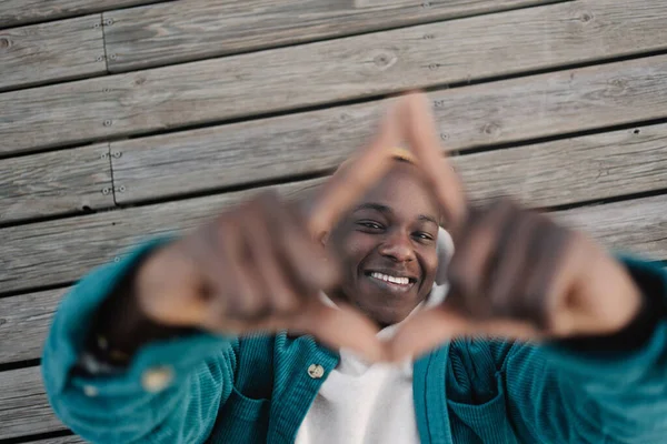 Lystig svart mann lager rammeskilt med begge hender som ser mot kameraet med smil. – stockfoto