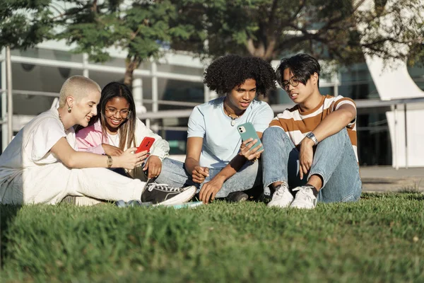 Grupper av glade, unge universitetsstudenter som ser på mobiltelefon i parken – stockfoto