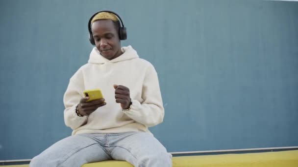 Kulaklıkla müzik dinlemek için akıllı telefon kullanan modacı Afrikalı Amerikalı adam. Gülümseyen Havalı Siyah Dans İnternet müzik uygulaması — Stok video