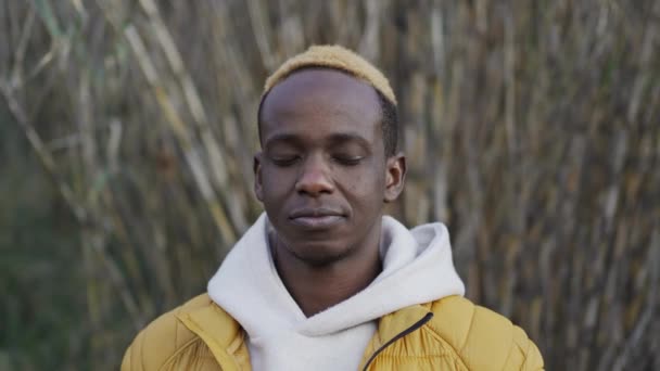 Mladý Afričan otevře zavřené oči, podívá se do kamery a usměje se nad vegetací. Portrétní lidský pozitivní výraz — Stock video