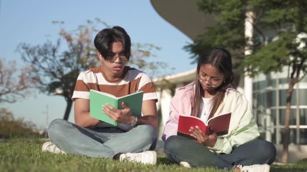 Dva univerzitní studenti sedící na trávě vysokoškolského kampusu a studující společně knihu — Stock video