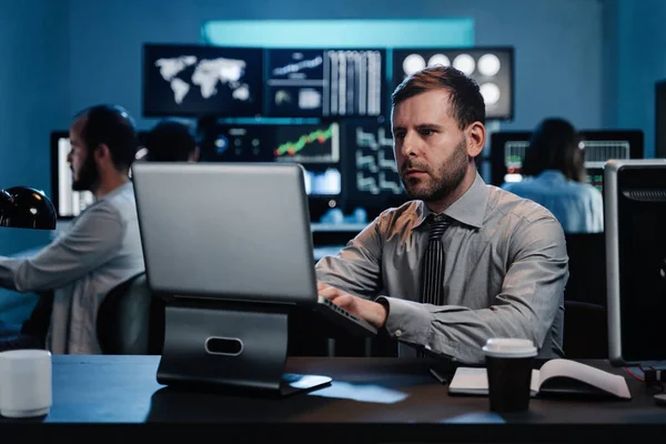 Mies elinkeinonharjoittaja istuu toimistossa työskentelee kannettavan tietokoneen seuranta osakemarkkinoilla tarkastellaan monitorit analysoida hintakehitystä — kuvapankkivalokuva