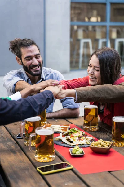 Jongeren die hun handen ineen slaan terwijl ze plezier hebben met drinken in een bar. Vrienden met stapels handen die vriendschap en teamwork tonen — Stockfoto