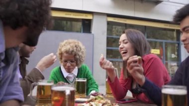 Mutlu genç modern arkadaşlar birlikte vakit geçiriyorlar tapas yiyorlar ve açık hava barında bira içiyorlar. Tatil tatilini kutluyorlar.