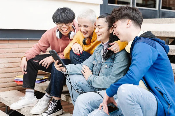 Unge tenåringsvenner som bruker mobiler og sosiale medier Studenter som sitter på campus og deler morsom video på smarttelefonene – stockfoto