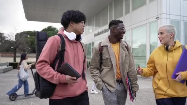 Tres jóvenes amigos estudiantes de raza mixta caminando por el campus universitario compartiendo historias riendo disfrutando de la juventud y la amistad. Diversidad en la enseñanza superior — Vídeo de stock